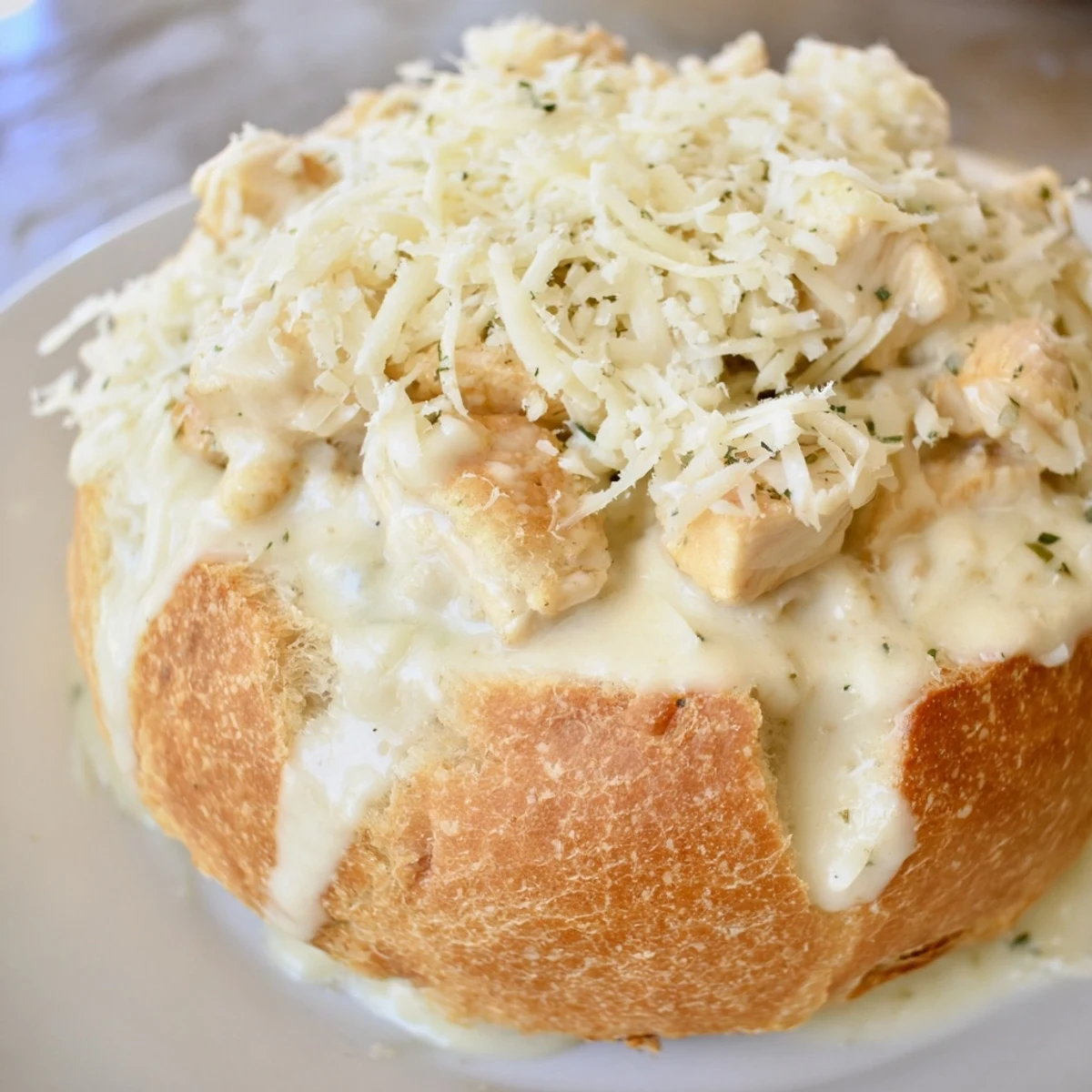 Freshly baked bread holds rich, steaming Chicken Alfredo, garnished with green parsley for serving.
