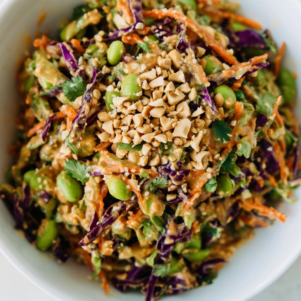 The Crunchy Thai Peanut Salad is served in a white bowl with lime wedges, highlighting its colorful, fresh ingredients for a light vegetarian meal.  