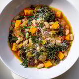 Close-up of a rustic Italian Bean & Kale Stew, perfectly garnished with fresh parsley and Parmesan.