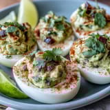 Classic deviled eggs filled with smooth guacamole, garnished with smoked paprika and cilantro for vibrant flavor.