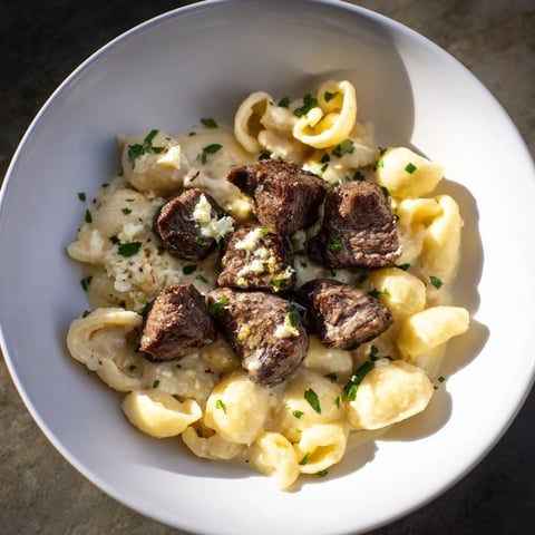 Garlic butter steak bites glistening from the skillet, served alongside creamy, cheesy pasta shells.