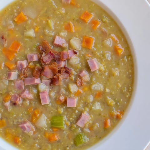 Steaming bowl of Split Pea Soup brimming with ham and bacon, ready to enjoy on a cold day.