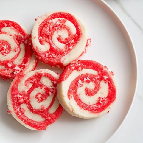 Swirled red and white Candy Cane Pinwheel Cookies, perfect for holiday baking, offer a sweet peppermint aroma.