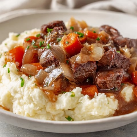 Steam rises from a hearty bowl of fall apple cider beef stew served over mashed potatoes.