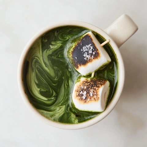 Steaming mug of toasted marshmallow campfire matcha hot cocoa, topped with gooey, golden marshmallows.