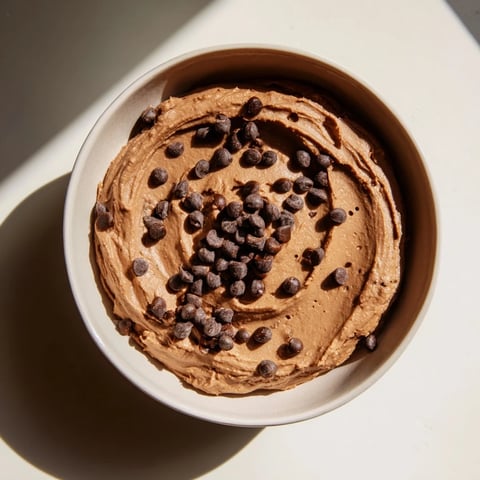 A bowl of rich, smooth chocolate hummus ready to be scooped with fresh strawberries.
