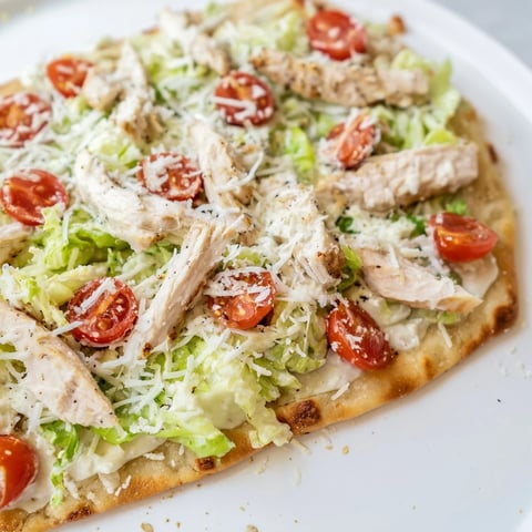 A close-up view of a crispy Chicken Caesar Flatbread topped with juicy grilled chicken, fresh romaine, and grated parmesan.