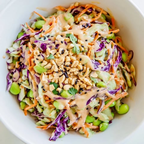 A close-up of Crunchy Thai Peanut Salad featuring vibrant purple cabbage, shredded carrots, and edamame in a creamy peanut dressing, topped with chopped peanuts and cilantro.  