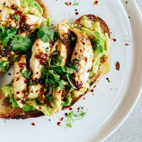 Golden grilled chicken slices layered over creamy smashed avocado on toasted sourdough, topped with chili flakes and a honey drizzle.