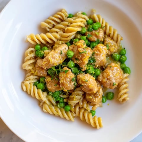 Tender chicken pieces and sweet peas tossed in rich garlic butter sauce over curly pasta, garnished with fresh parsley and lemon zest.
