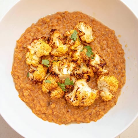 A bowl of steaming dhal with cumin-roasted cauliflower, garnished with fresh cilantro and served with basmati rice.
