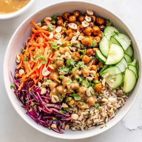 A close-up of a Peanut Chickpea Rice Bowl drizzled with creamy sauce and garnished with green onions.