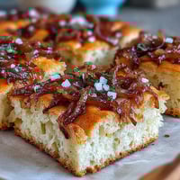 A golden sourdough focaccia topped with sweet caramelized onions and a sprinkle of flaky sea salt, baked to perfection.