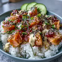 Spicy mayo salmon rice bowl with tender salmon cubes over fluffy rice, drizzled with creamy sriracha mayo and topped with crisp cucumber and sesame seeds.